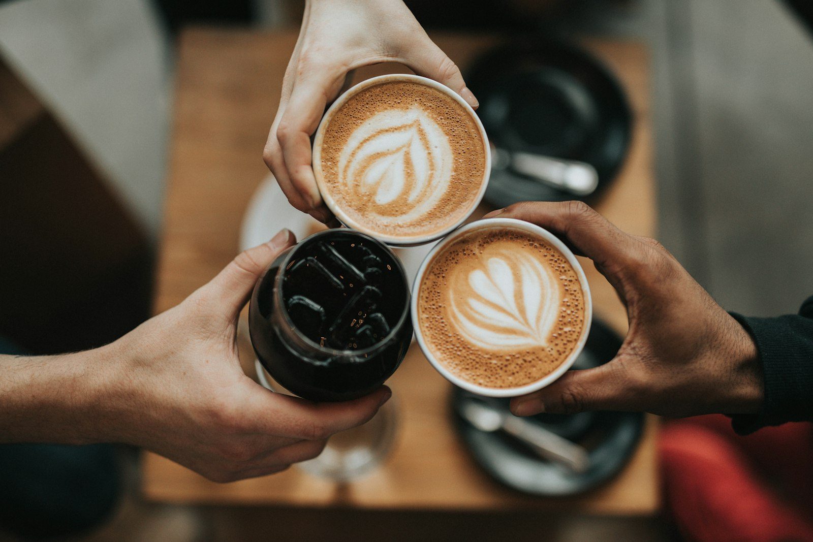 Tiga tangan mengangkat cangkir kopi bersulang di atas meja kedai