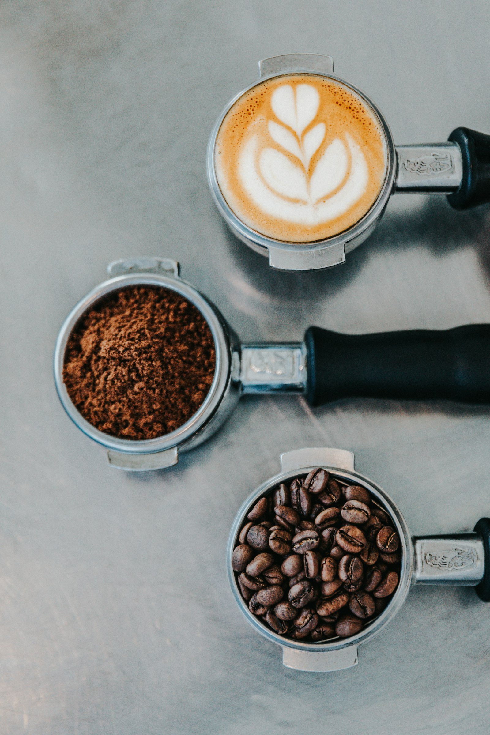 Portafilter berisi kopi baru digiling dan secangkir latte di atas meja kedai
